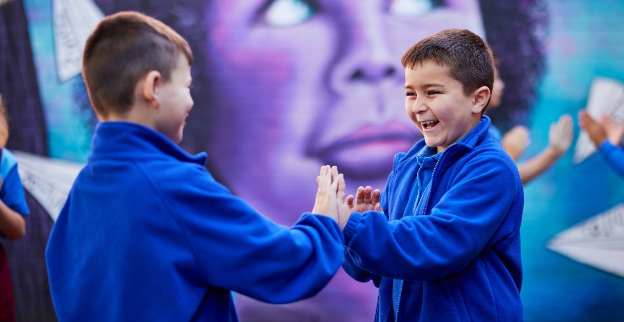Two boys in blue jumpers playing outside in front of a large mural.