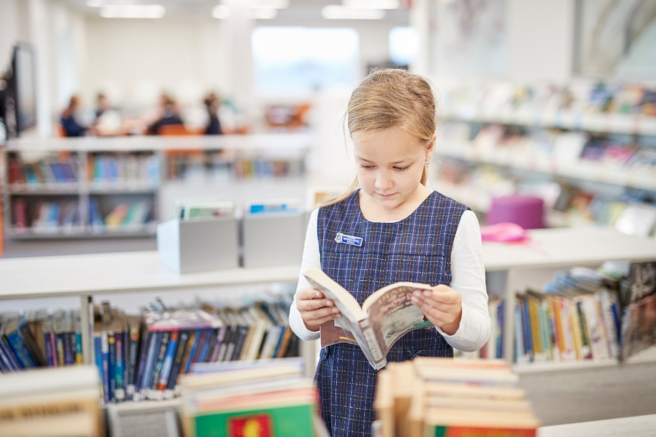 A young girl standing in a library reading a book