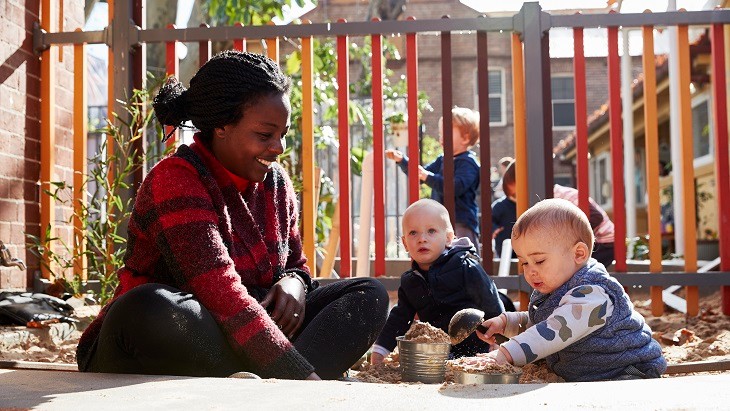 Teacher with two toddlers playing in a sandpit.
