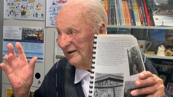 An elderly man holding up a book.